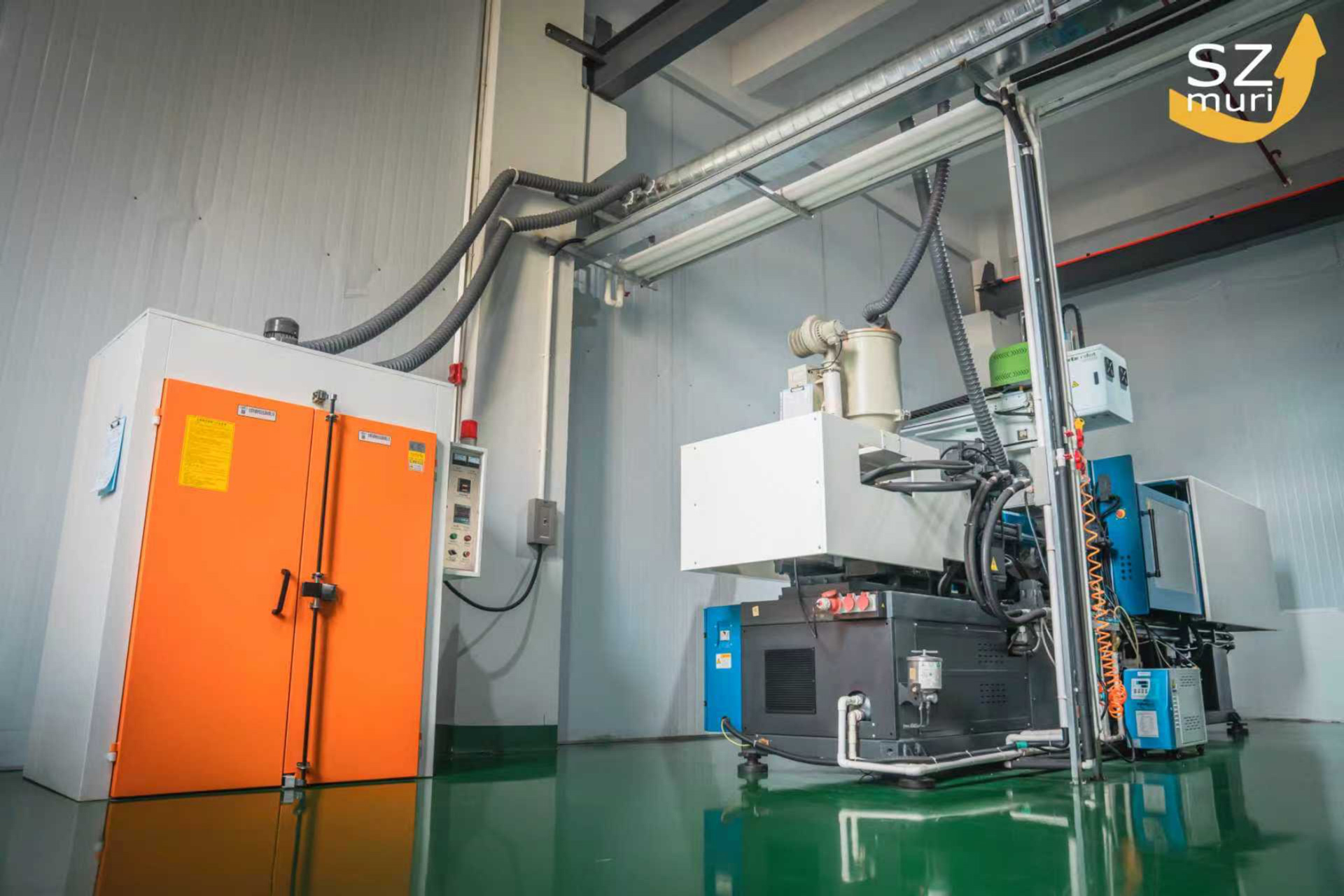 Industriemaschine mit weißen und orangen Elementen und glänzend grünem Boden