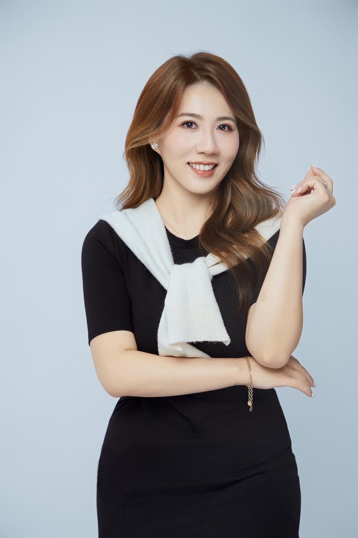 Junge Frau mit gewelltem braunem Haar lacht freundlich und trägt ein schwarzes Kleid mit weißem Pullover über den Schultern