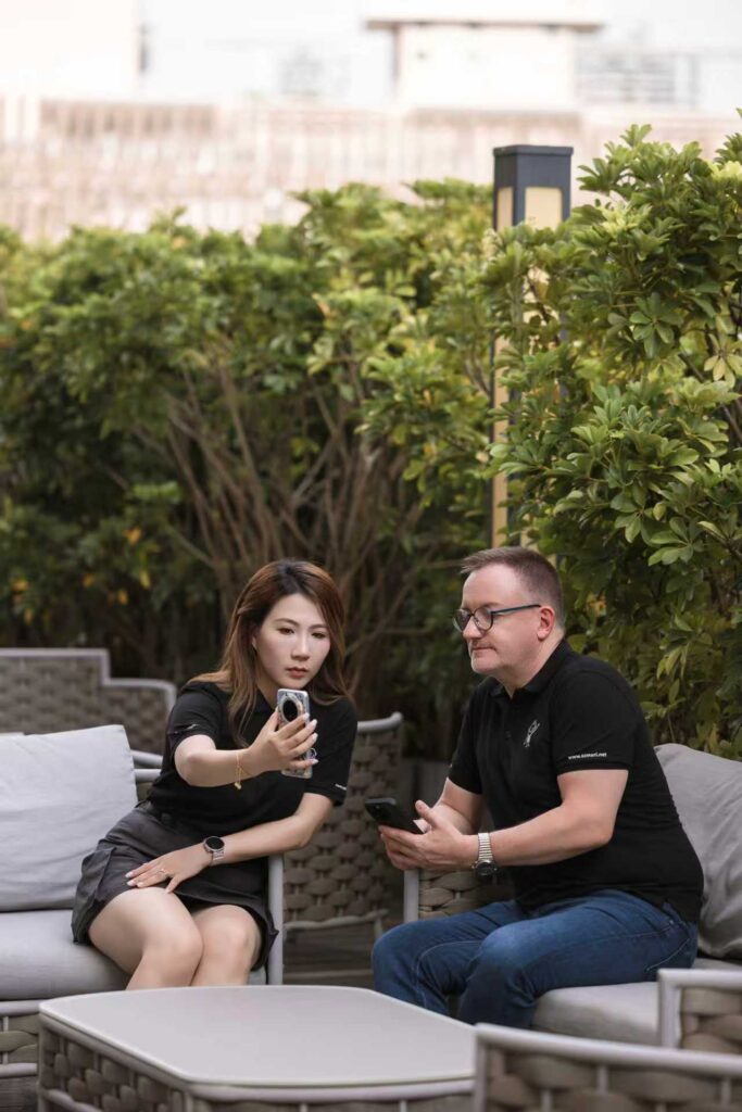 Eine Frau zeigt einem Mann draußen auf einem Sofa entspannt etwas auf ihrem Handy