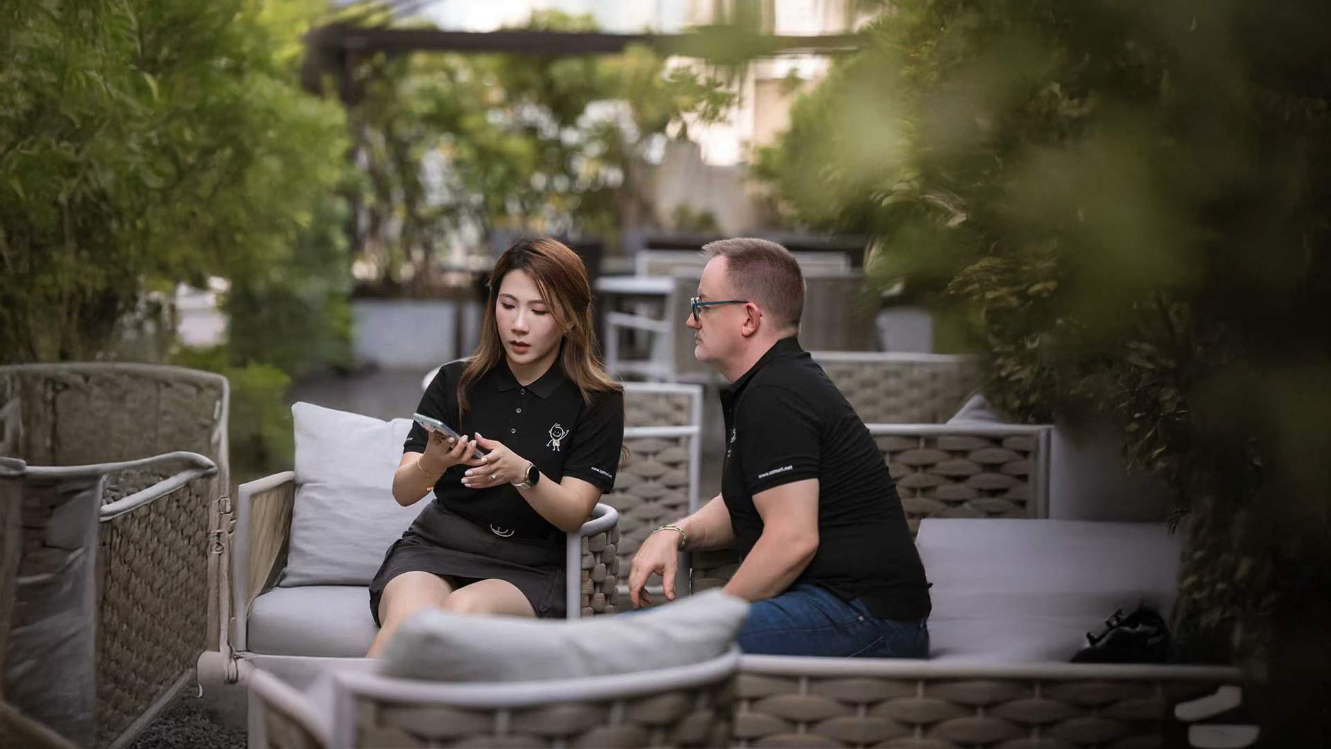 Eine junge Frau zeigt einem Mann etwas auf ihrem Smartphone in einem grünen Außenbereich